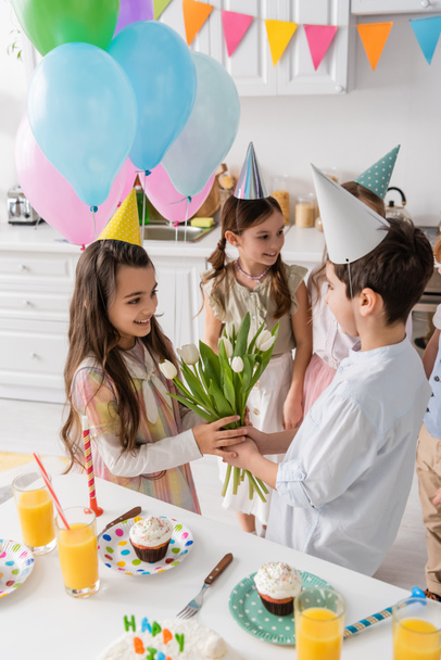 preteen boy giving tulips to cheerful birthday girl near kids on blurred background  - Photo, Image