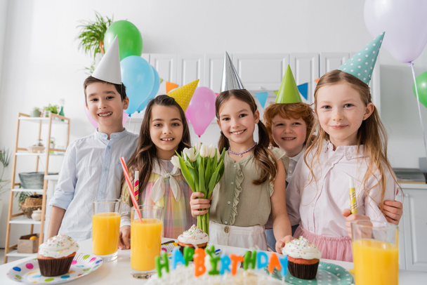 cheerful girl holding tulips near friends during birthday party at home  - Foto, imagen