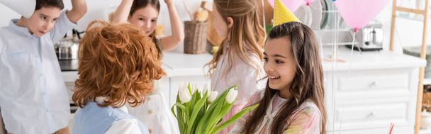 menina feliz em boné de festa levando tulipas de menino ruivo perto de amigos no fundo borrado, banner  - Foto, Imagem