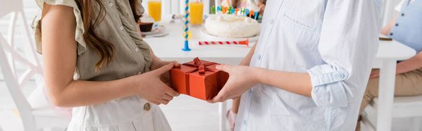 bijgesneden weergave van tiener jongen geven geschenk aan verjaardag meisje in de buurt van vrienden op wazige achtergrond, banner  - Foto, afbeelding