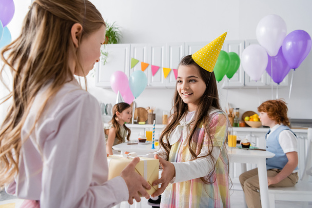 cheerful birthday girl receiving present from friend during birthday party  - Photo, Image