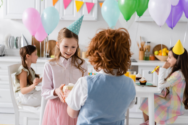 cheerful girl receiving present from redhead boy during birthday party  - Photo, Image
