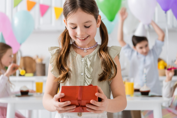 happy girl holding birthday present near friends on blurred background  - Photo, Image