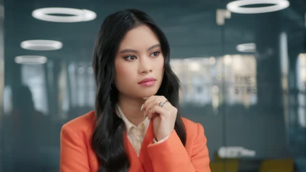 Pewna siebie młoda azjatycka stylowa bizneswoman stoi w biurze uważnie słuchając kolegi 4K. Skoncentrowany profesjonalna dziewczyna z ładnym włosy na twarzy pozowanie do zbliżenia portret w pomieszczeniach - Materiał filmowy, wideo