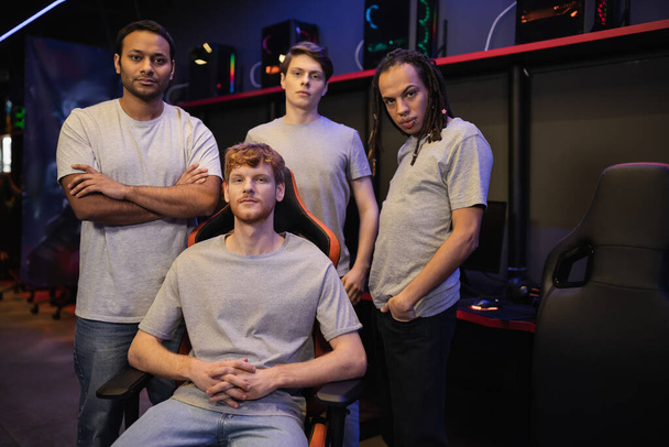 Multiethnisches Gamer-Team in grauen T-Shirts blickt in Cyber-Club in die Kamera  - Foto, Bild