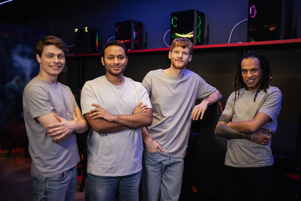 Positieve multi-etnische team van gamers op zoek naar camera in cyber club  - Foto, afbeelding