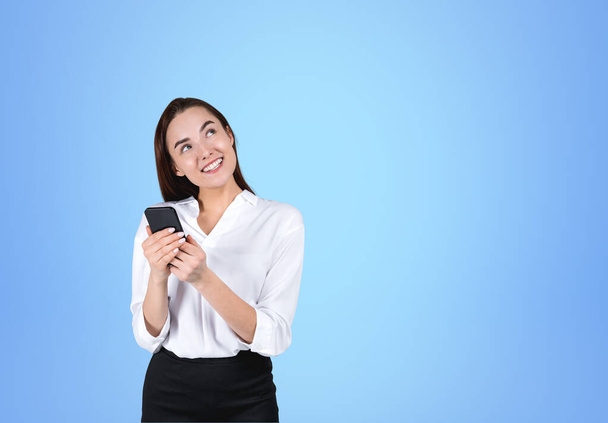 Smiling businesswoman working with phone, online browse internet and thinking on blue background. Concept of communication and social media. Copy space - Foto, Bild