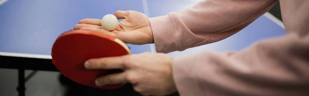 Oyun kulübünde masa tenisi oynarken top ve raket tutan adamın kırpılmış görüntüsü.  - Fotoğraf, Görsel