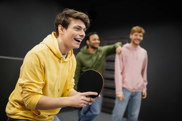 Cheerful man playing table tennis near blurred friends in gaming club  - Foto, Bild