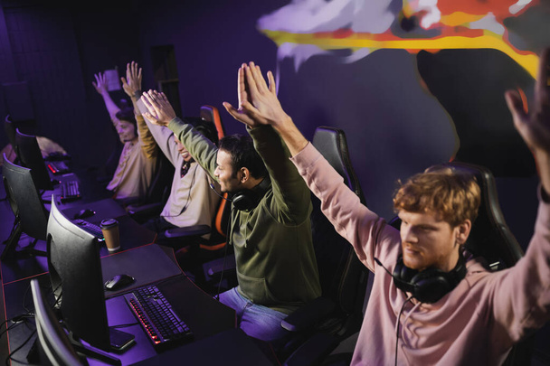 Smiling indian man giving high five to friends near computers in gaming club  - Photo, Image