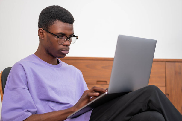 Serious African American businessman wearing casual wear is sitting working on laptop holding it on his lap. Concept of distant, online, remote learning, business education - Zdjęcie, obraz
