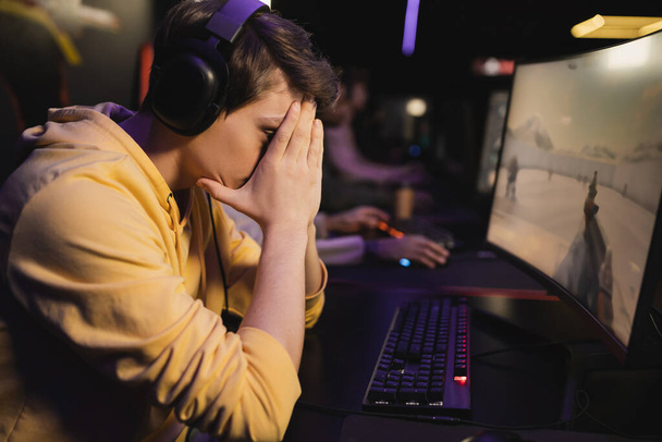 Triste jugador de auriculares sentado cerca de la computadora en el club de juego  - Foto, imagen