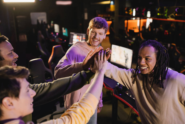 Hohe Blickwinkel auf positive multiethnische Freunde geben High Five in Gaming Club  - Foto, Bild