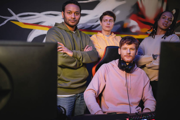 Multiethnische Gamer blicken in Spielklub auf Kamera in der Nähe von Computern  - Foto, Bild