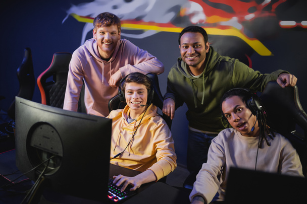 Multiethnische Gamer lächeln in die Kamera in der Nähe von Computern im Gaming Club  - Foto, Bild