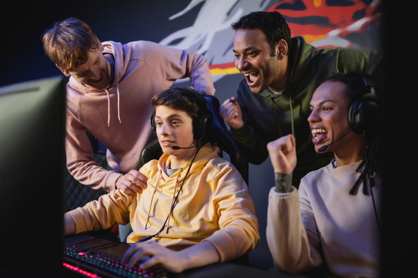 Nadšený mezirasový tým při pohledu na přítele hraní videohry na počítači v kybernetickém klubu  - Fotografie, Obrázek