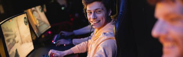 Jugador sonriente en auriculares mirando a un amigo borroso en blub de juegos, banner  - Foto, Imagen