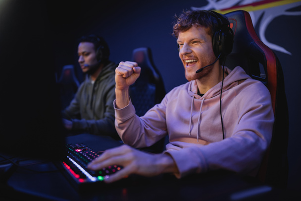 Izgalmas játékos a fejhallgató mikrofon mutatja igen gesztus számítógép közelében cyber klub  - Fotó, kép