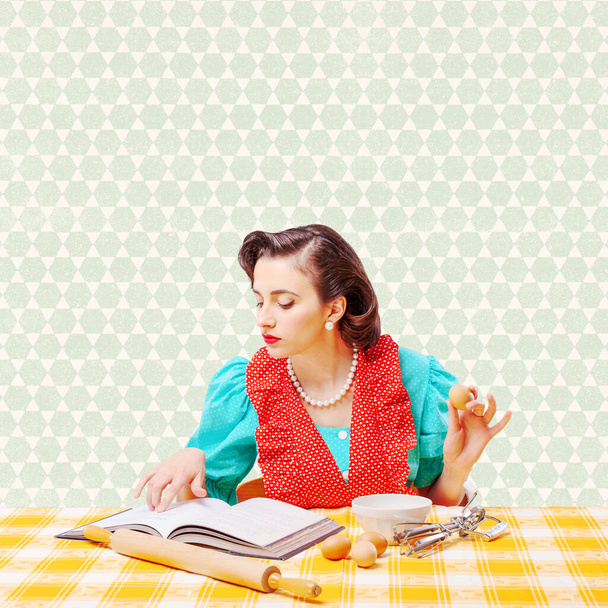 Beautiful vintage style housewife preparing a dessert at home, she is checking the recipe in a cookbook and mixing ingredients in a bowl - Фото, изображение