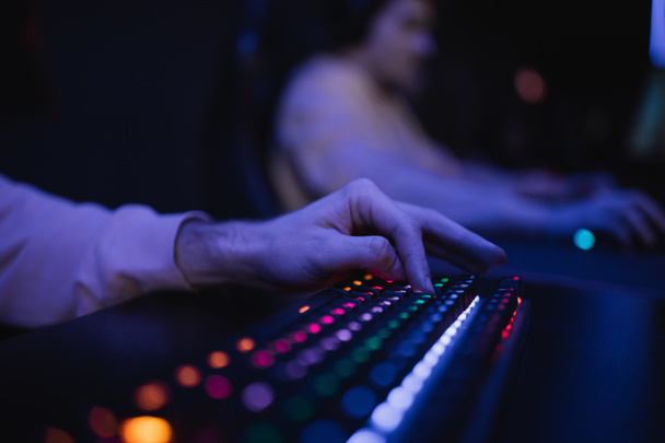 Vista ritagliata del giocatore utilizzando la tastiera con illuminazione colorata nel club di gioco  - Foto, immagini