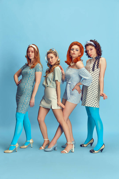 Fashion show. Full-length portrait of beautiful young women posing in stylish clothes against blue studio background. Concept of retro style, fashion, beauty, elegance, 60s, youth. Pin-up style - Foto, afbeelding
