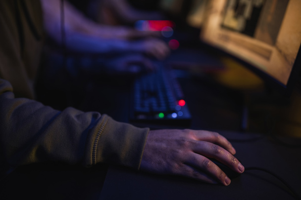 Oříznutý pohled na hráče sedícího poblíž rozmazaného počítače v kybernetickém klubu  - Fotografie, Obrázek