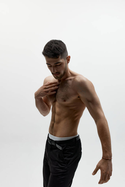 Aesthetics of male body. Portrait of handsome young muscular guy, man posing shirtless over white studio background. Masculinity and strength. Concept of mens health, beauty of male body - Foto, Imagen