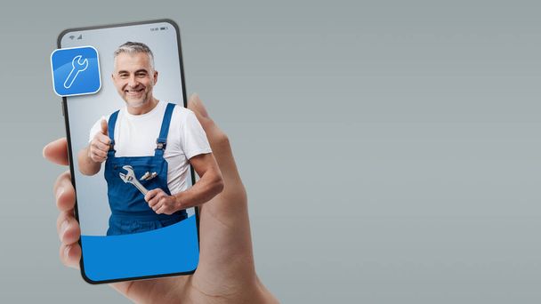 Professional plumber and repairman on smartphone screen: hire contractors online - Fotó, kép