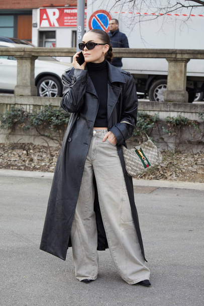 MILAN, ITALY - FEBRUARY 24, 2023: Woman with black leather trench coat and Gucci Balenciaga bag before Sportmax fashion show, Milan Fashion Week street style - Foto, Imagen