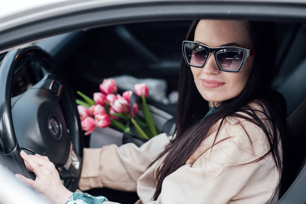 女性中心の車のカスタマイズ。女性のニーズや好みに特化した車を設計します。女性に焦点を当てた車の安全機能。チューリップの花の花束を持つ女性が車に乗り込む. - 写真・画像