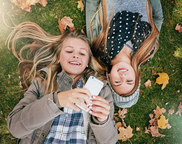 Co robią nasi przyjaciele? Wysoki kąt ujęcia dwóch szczęśliwych nastolatków relaksujących się razem na trawie na zewnątrz - Zdjęcie, obraz