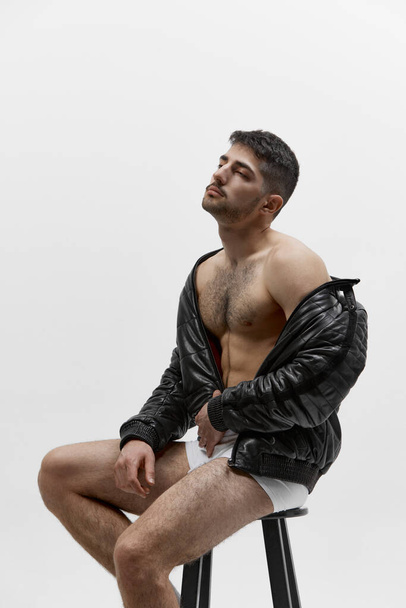 Muscular body shape. Half length portrait of young attractive man wearing leather jacket on naked body over light studio background. Concept of mens fashion, health, beauty of male body - Fotó, kép