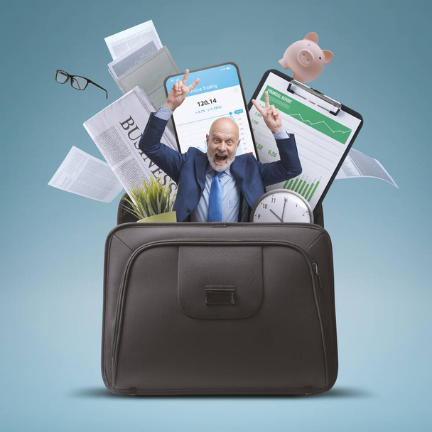 Cheerful businessman celebrating with arms raised and office items in a briefcase: successful business and investments concept - Photo, Image