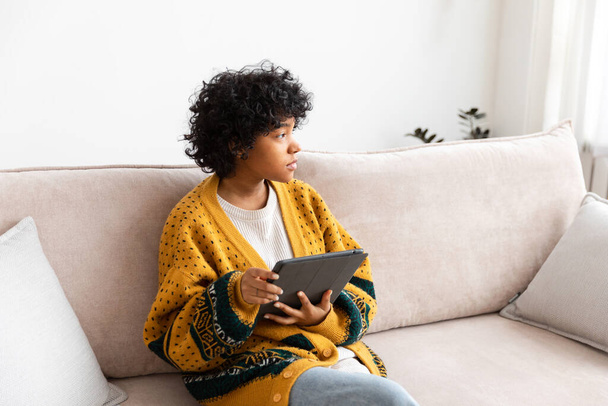 African American girl holding digital tablet οθόνη αφής πληκτρολόγηση σελίδα πάπυρο στο σπίτι. Γυναίκα με mobile tech συσκευή surfing internet χρησιμοποιώντας εφαρμογές κοινωνικής δικτύωσης παίζοντας παιχνίδι. Εργασίες μελέτης ψώνια online - Φωτογραφία, εικόνα