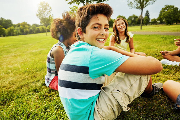 Mí přátelé jsou naprosto úžasní. Portrét mladého chlapce sedícího s přáteli na trávě venku - Fotografie, Obrázek