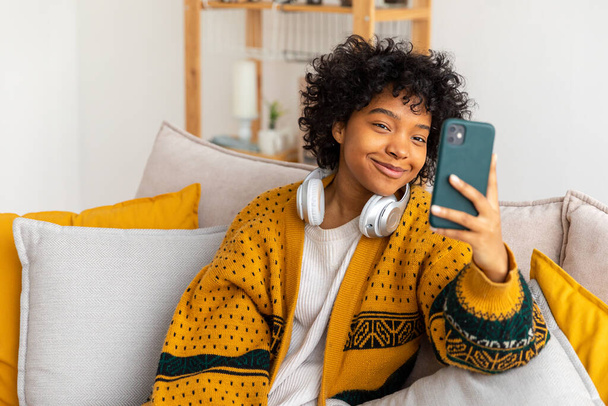Afroamerykanka trzymająca smartfona na video czacie. Blogerka rozmawiająca z najlepszymi przyjaciółmi w sieci społecznościowej. Młoda kobieta o wirtualnym spotkaniu online czat wideo rozmowy w domu - Zdjęcie, obraz