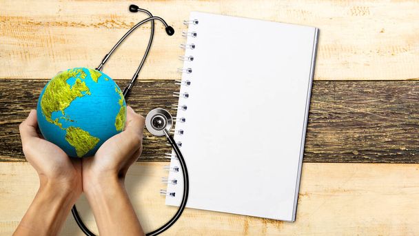Die menschliche Hand hält die Erde mit einem Stethoskop und einem leeren Notizbuch. Konzept zum Weltblutdrucktag - Foto, Bild
