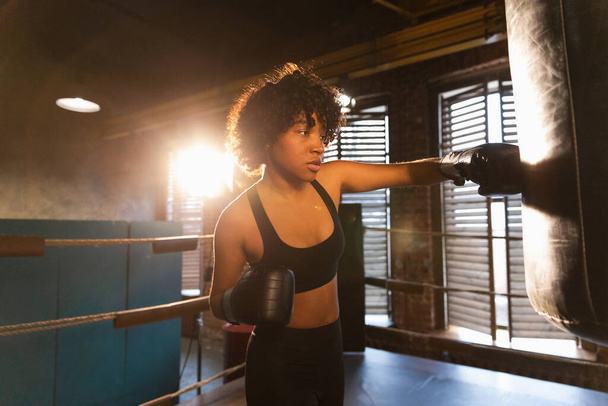 Kadın kendini savunma gücü. Afrika kökenli Amerikalı kadın boks ringinde boks eğitimi veriyor. Sağlıklı, boks torbası yumruklayan güçlü bir kız. Boks salonunda antrenman günü. Vücut çalıştırma eğitimine uygun güç - Fotoğraf, Görsel