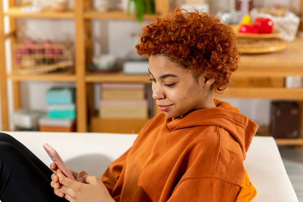 African girl holding smartphone touch screen typing scroll page at home. Woman with cell phone surfing internet using social media apps playing game. Shopping online Internet news cellphone addiction - Foto, afbeelding
