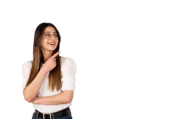 Pointing copy space, portrait of excited girl pointing copy space. Isolated white background. Brunette caucasian young woman smiling and showing with her finger. Advertising concept idea. - 写真・画像