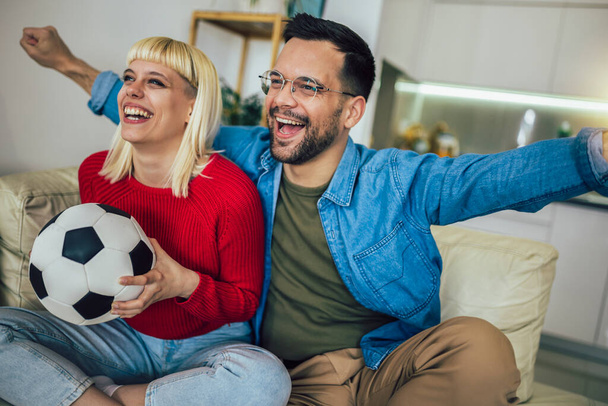 Fiatal pár néz egy focimeccset a televízióban az otthonuk kényelméből. - Fotó, kép