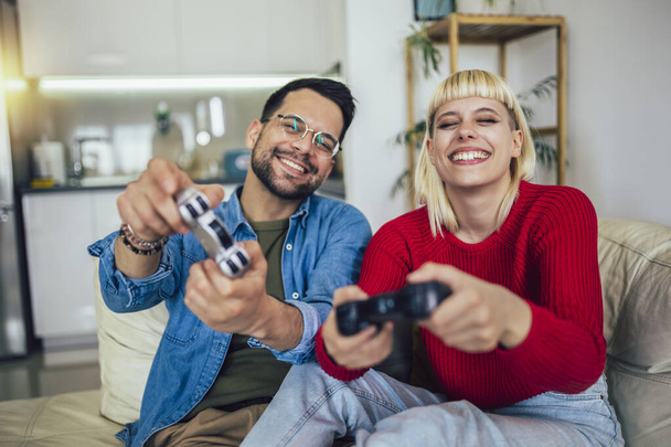 Chłopak i dziewczyna grają w gry wideo z joystickami w salonie. Kochająca się para gra w gry wideo w domu - Zdjęcie, obraz