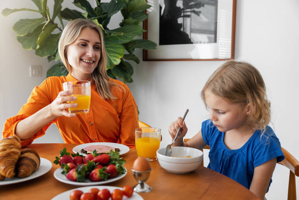 mother and daughter eating breakfast at home. sitting by the table in the kitchen - Foto, imagen