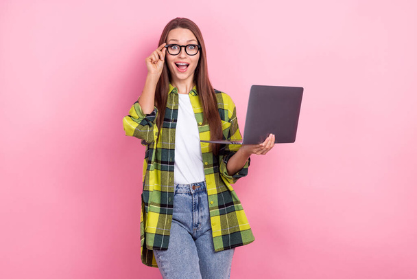 Portret van grappig onder de indruk meisje met rechte kapsel dragen geruite shirt houden laptop touch bril geïsoleerd op roze kleur achtergrond. - Foto, afbeelding