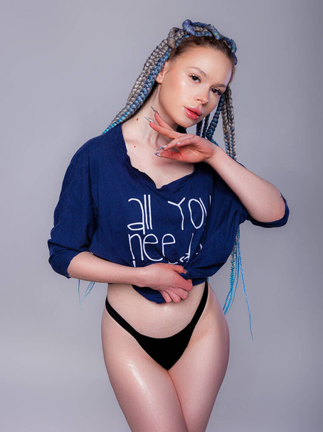 Young beautiful female with long pigtails hairstyle wearing oversize t-shirt and black panties posing against gray background. Studio shot copy space - Photo, Image