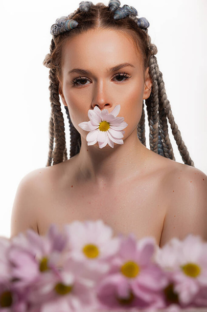 Schoonheidsportret van jonge vrouw met gezonde huid en roze bloemen in de buurt van gezicht - geïsoleerd op wit. Schattig gezicht voor gezondheid of schoonheidsproducten - Foto, afbeelding