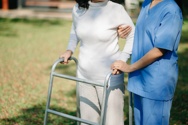 Asian careful caregiver or nurse and the happy patient  are walking in the garden to help and encourage and rest your mind with green nature. Help support yourself to learn to walk.  - Φωτογραφία, εικόνα