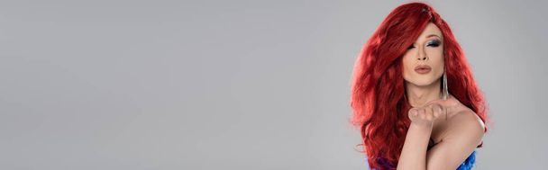 Drag queen in red wig blowing air kiss at camera isolated on grey, banner  - Foto, afbeelding