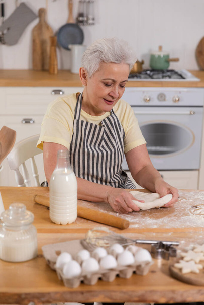 Boldog végzős nő főz a konyhában. Stílusos idősebb érett ősz hajú hölgy nagymama knead tészta sütit sütni. Az öreg nagyi házi készítésű ételt főz. Háziasszony-házimunka fogalma - Fotó, kép
