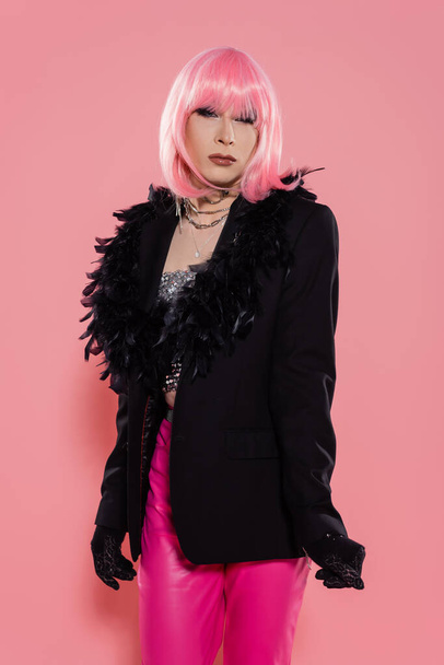 Portrait of drag queen in gloves and jacket looking at camera on pink background  - 写真・画像